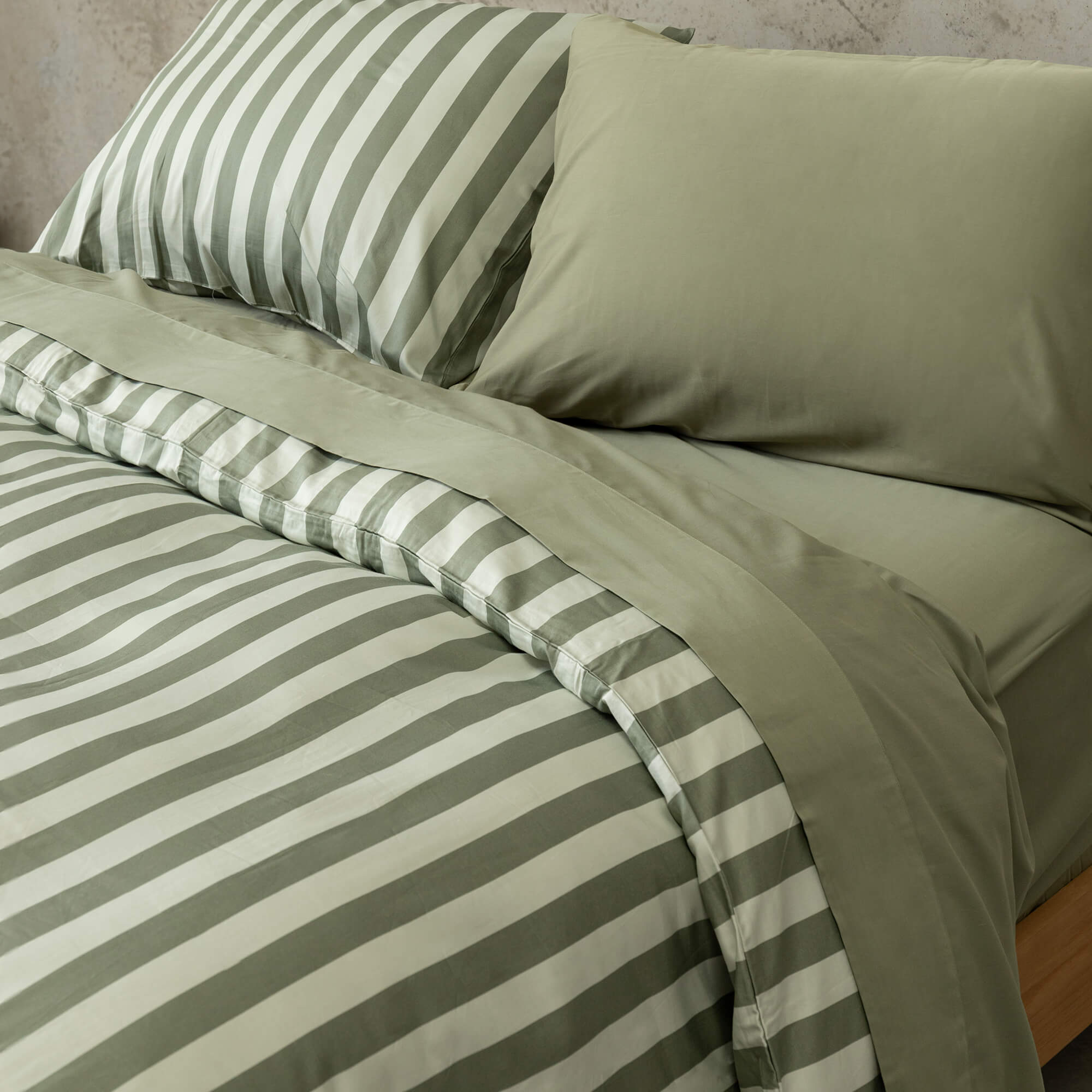Close up of a sage green and light green stripe quilt cover set on a bed, with sage green sheets and pillowcases.