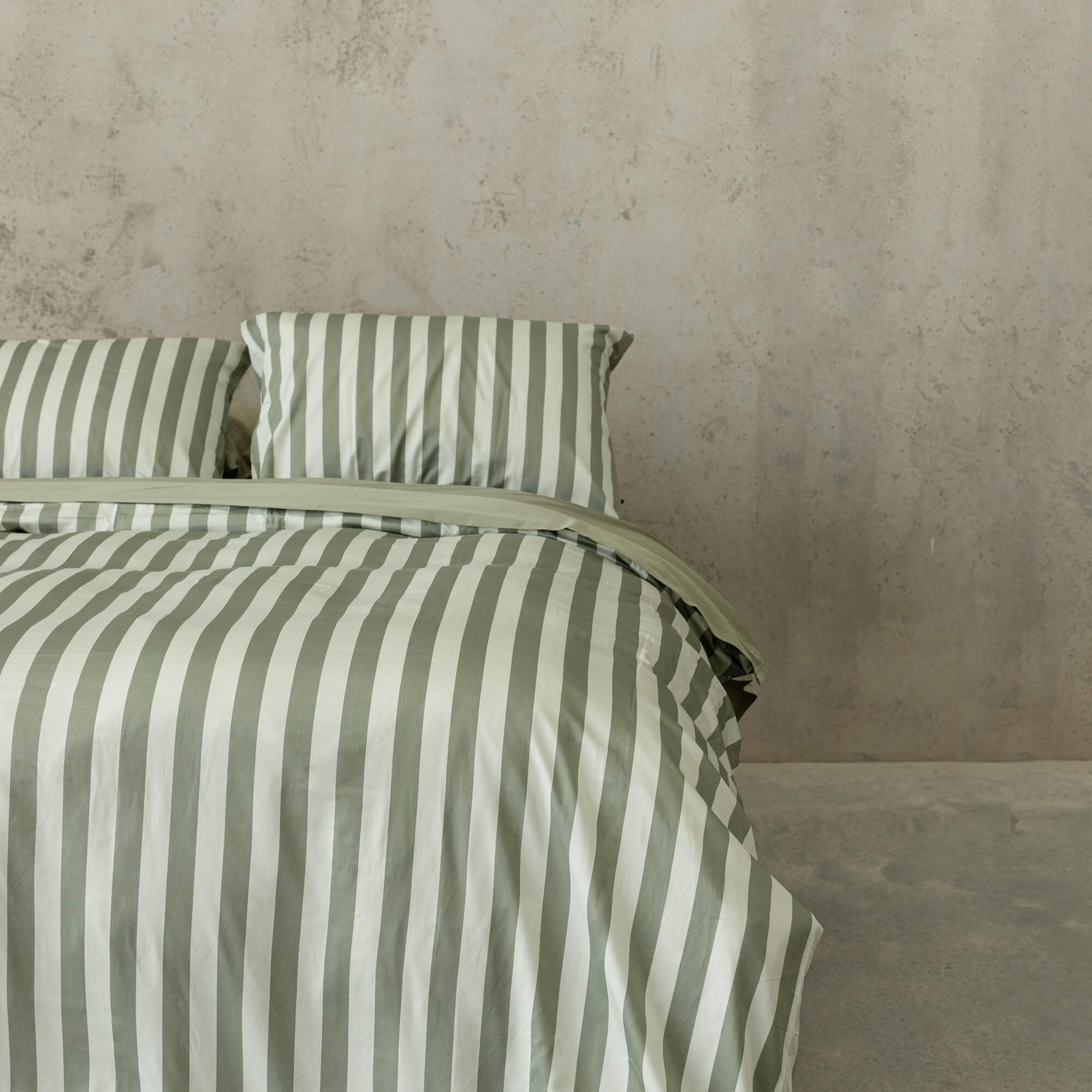 Close up of a sage green and light green stripe quilt cover set on a bed, with sage green sheets and pillowcases.