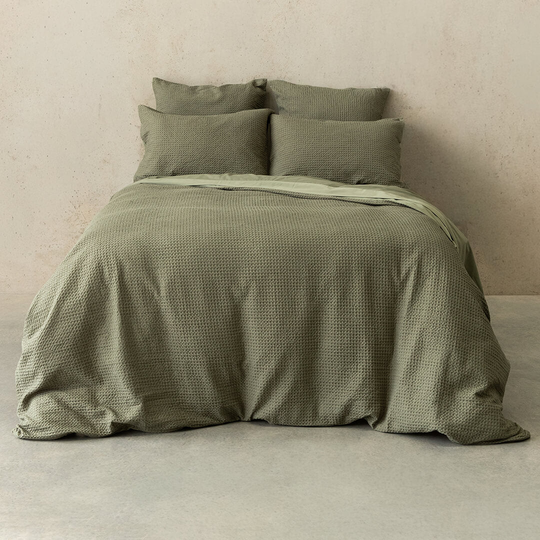 Green textured bedding set on a bed against a beige wall.