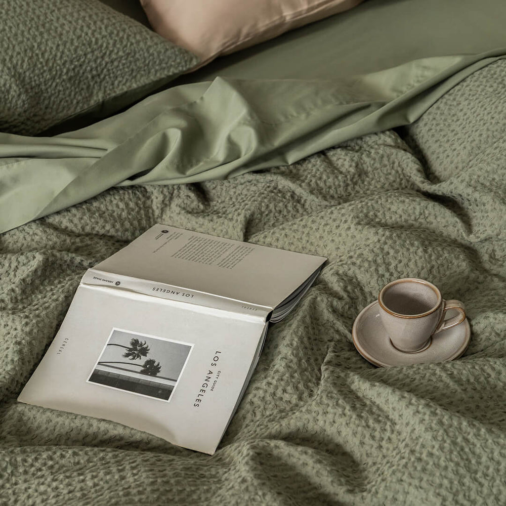 Book and cup on a textured green waffle quilt cover.