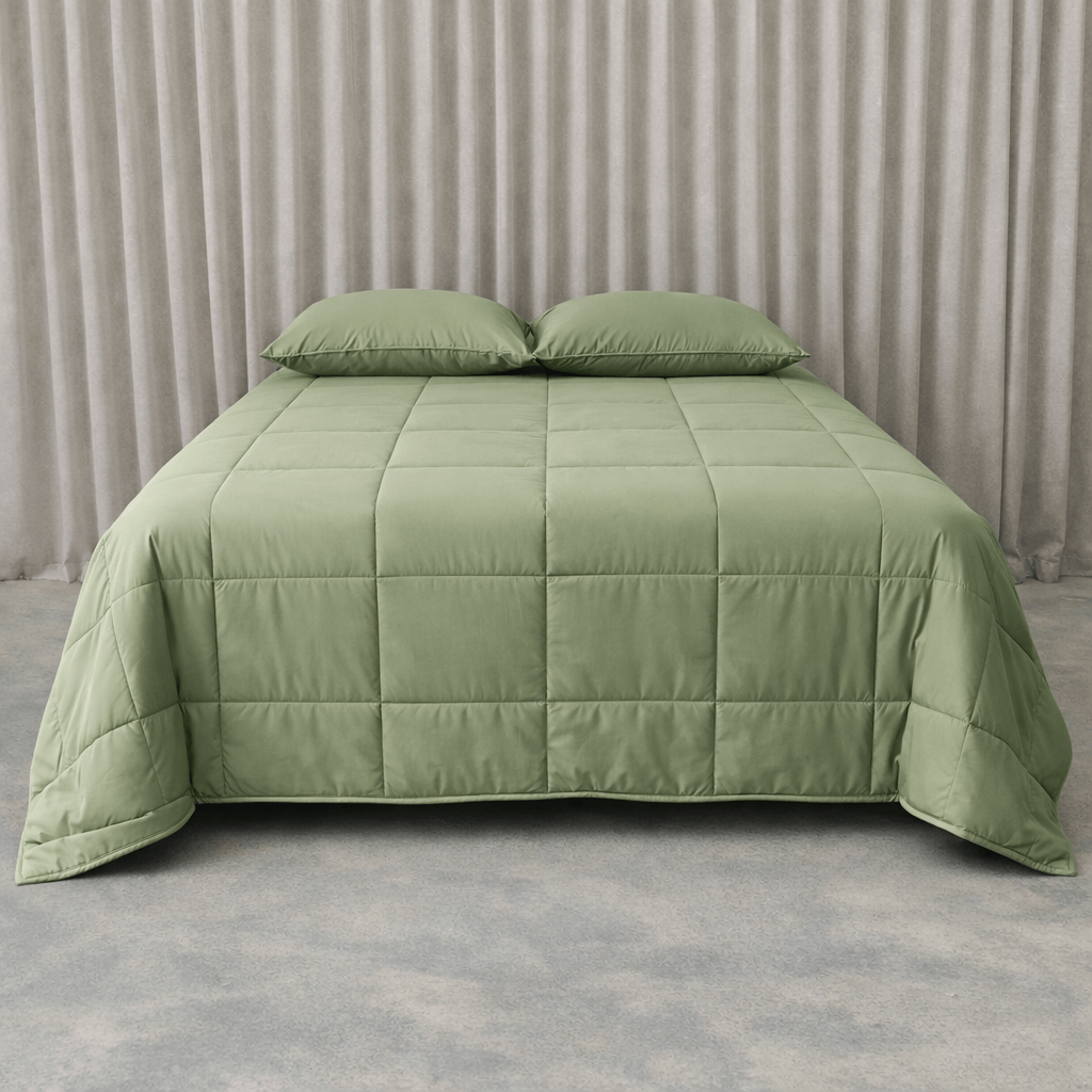 Green quilted cooling blanket on a bed with matching pillows against a neutral background.
