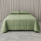Green quilted cooling blanket on a bed with matching pillows against a neutral background.