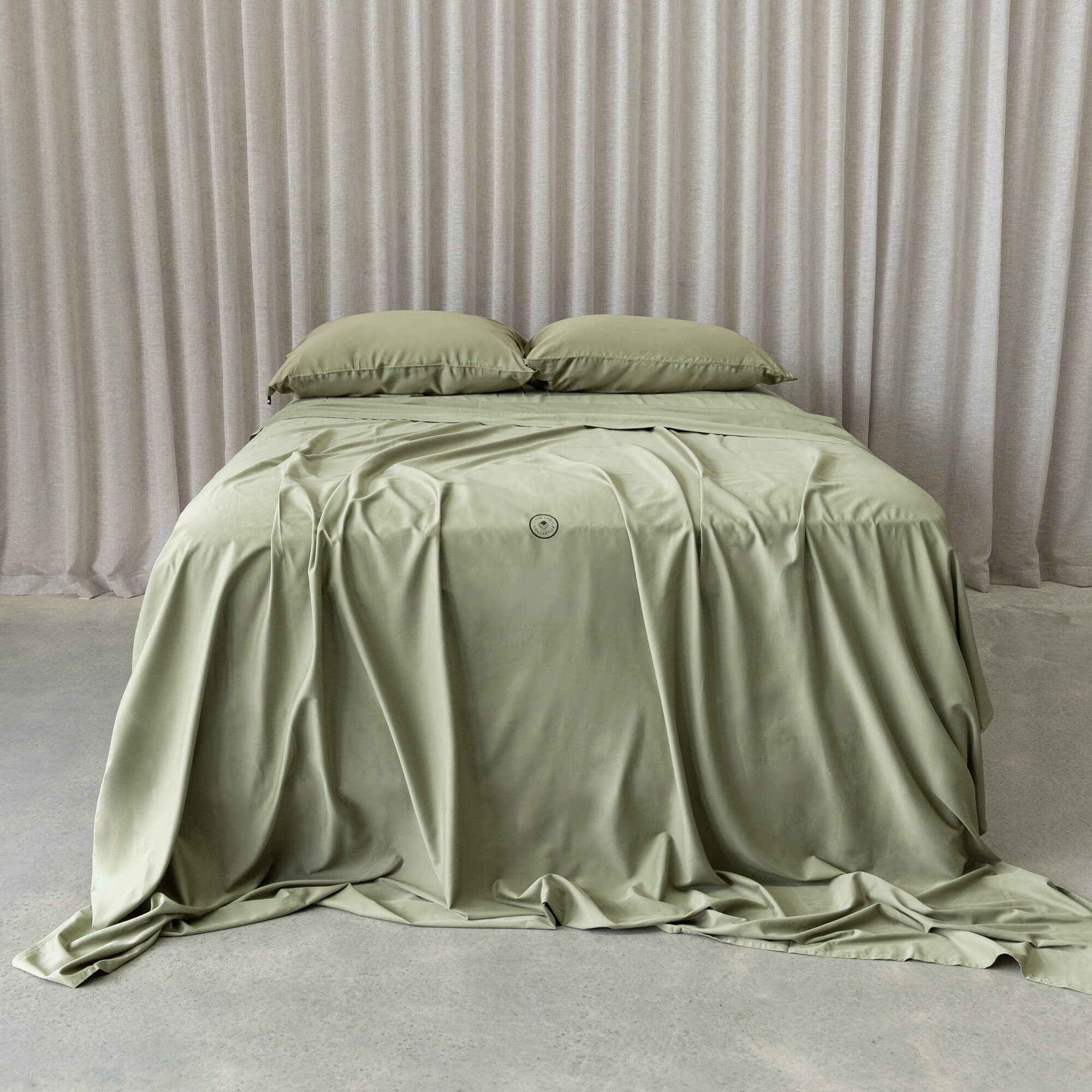 Sage green bedding set on a bed with a neutral curtain in the background.
