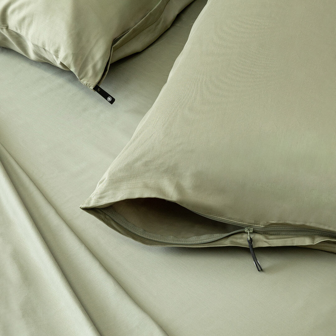 Close-up of green bedding with a zipper on pillowcases.