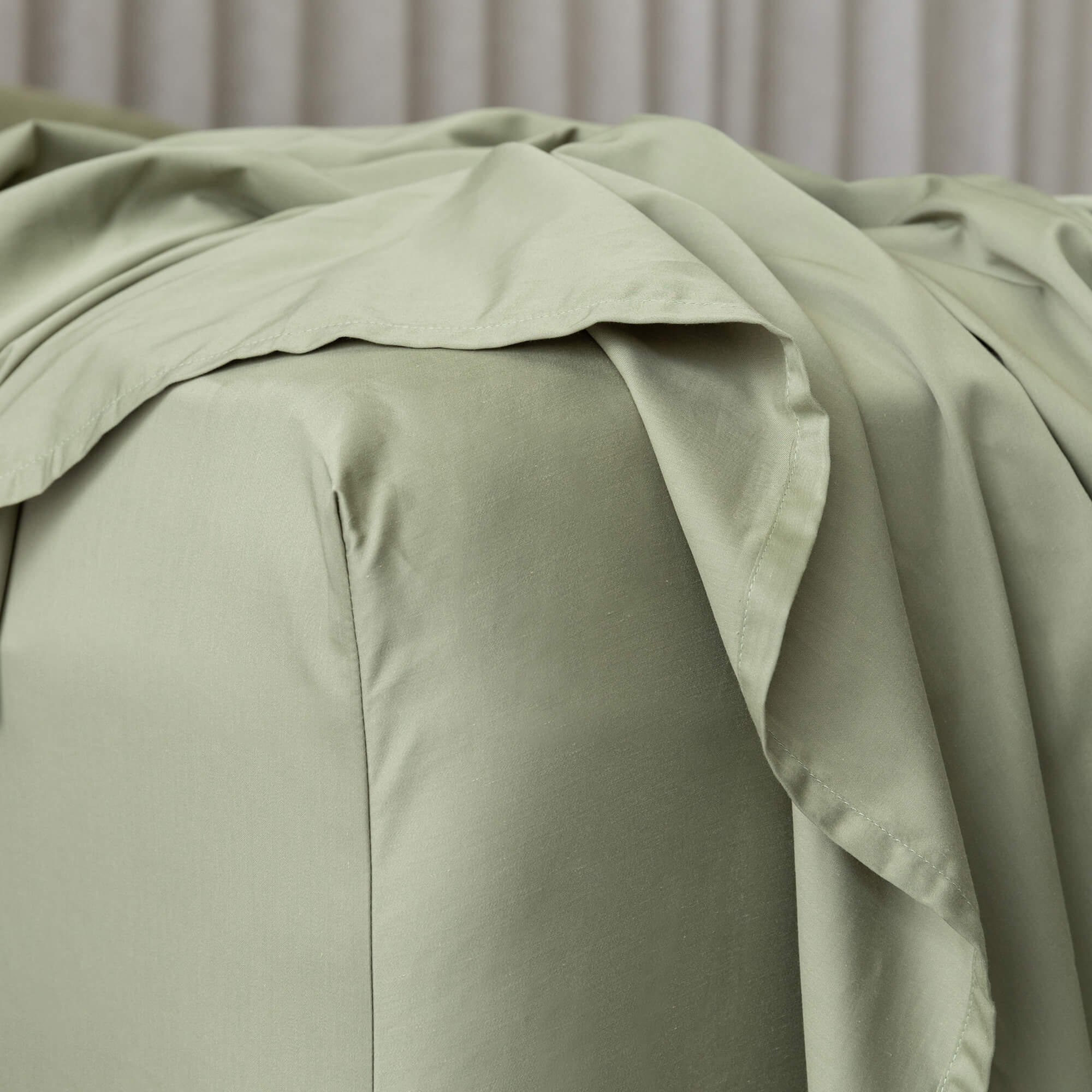 Close up of the corner of a sage green fitted sheet on a bed.