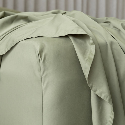 Green bed sheets on a bed with a neutral background.