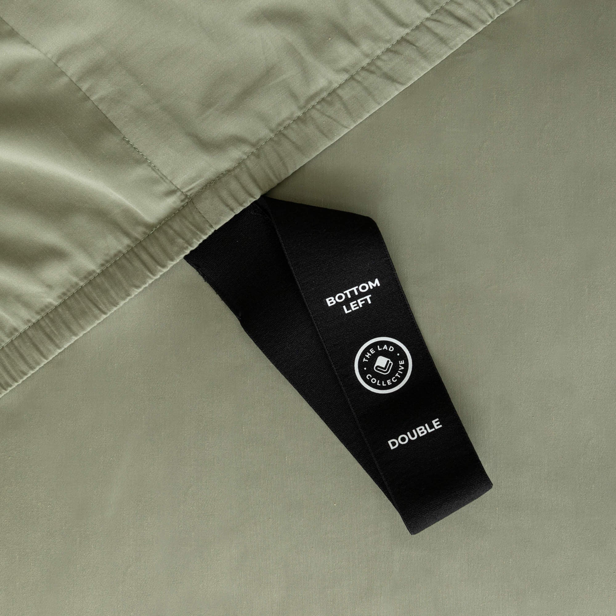 Sage green fitted sheet labelled corner loop strap that says 'Bottom Left' and 'Double'.
