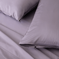 Close-up of lavender bedding with two matching pillows, including a zippered pillowcase and a small branded pull tab.