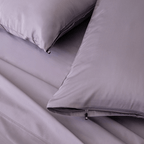 Close-up of lavender bedding with two matching pillows, including a zippered pillowcase and a small branded pull tab.