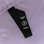 Close-up of a black corner strap attached to a lavender fitted sheet, labelled “Bottom Left” and “Double” for easy bed placement.