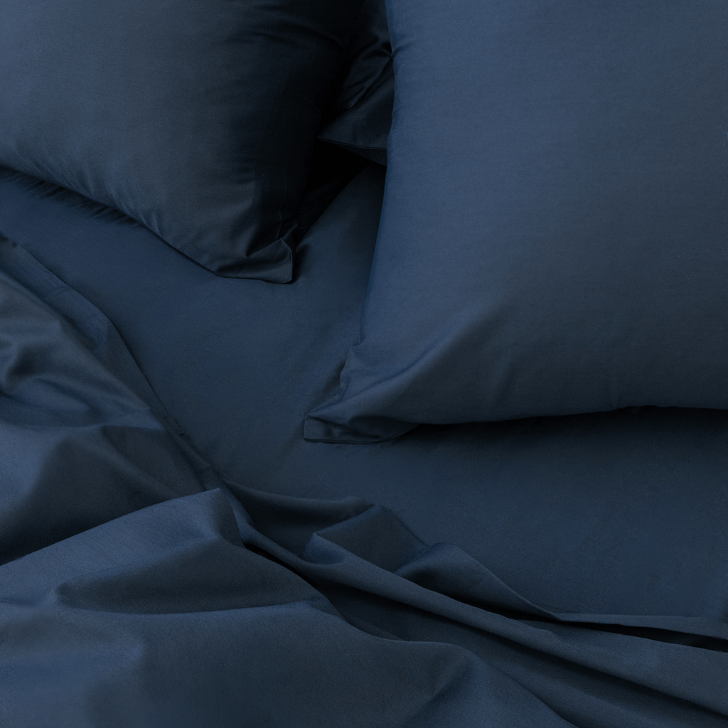 Close-up angle view of two navy blue pillowcases and a folded flat sheet on a bed