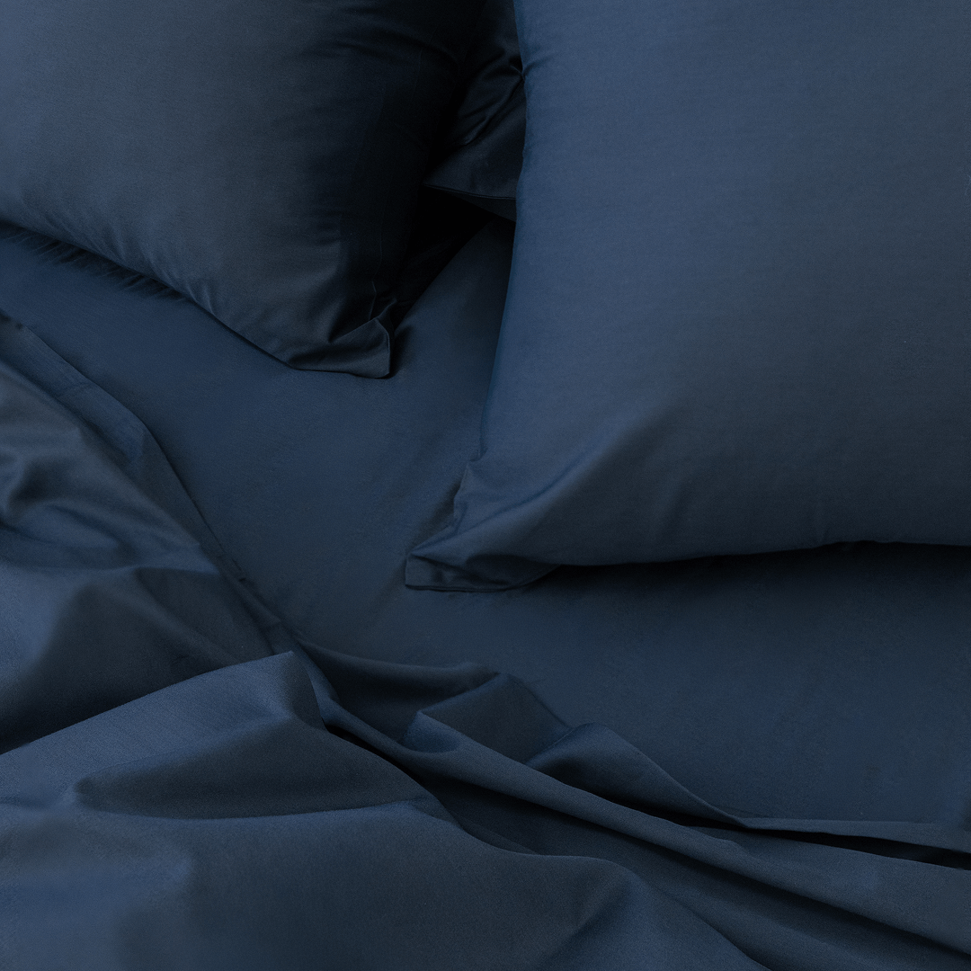 Close-up angle view of two navy blue pillowcases and a folded flat sheet on a bed