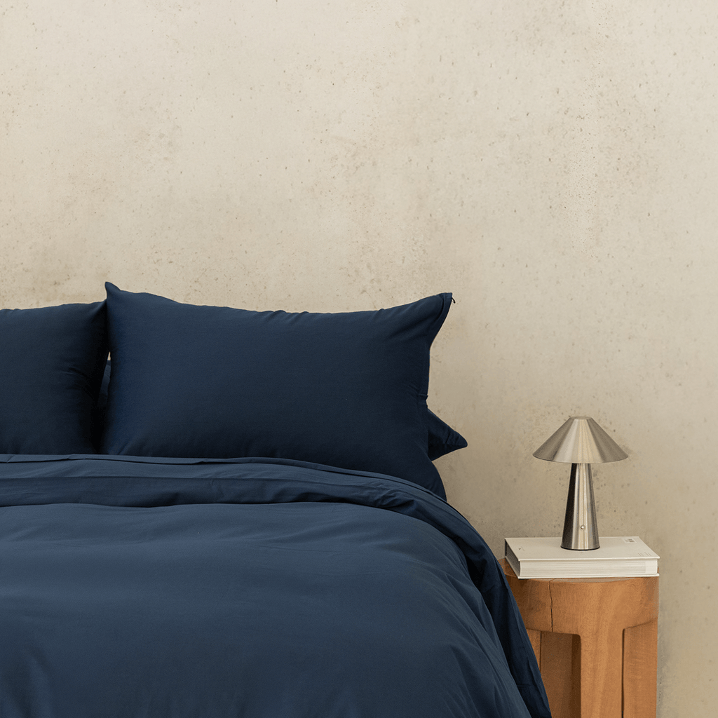 Front view of navy blue quilt bedding set with a wooden nightstand and metal table lamp