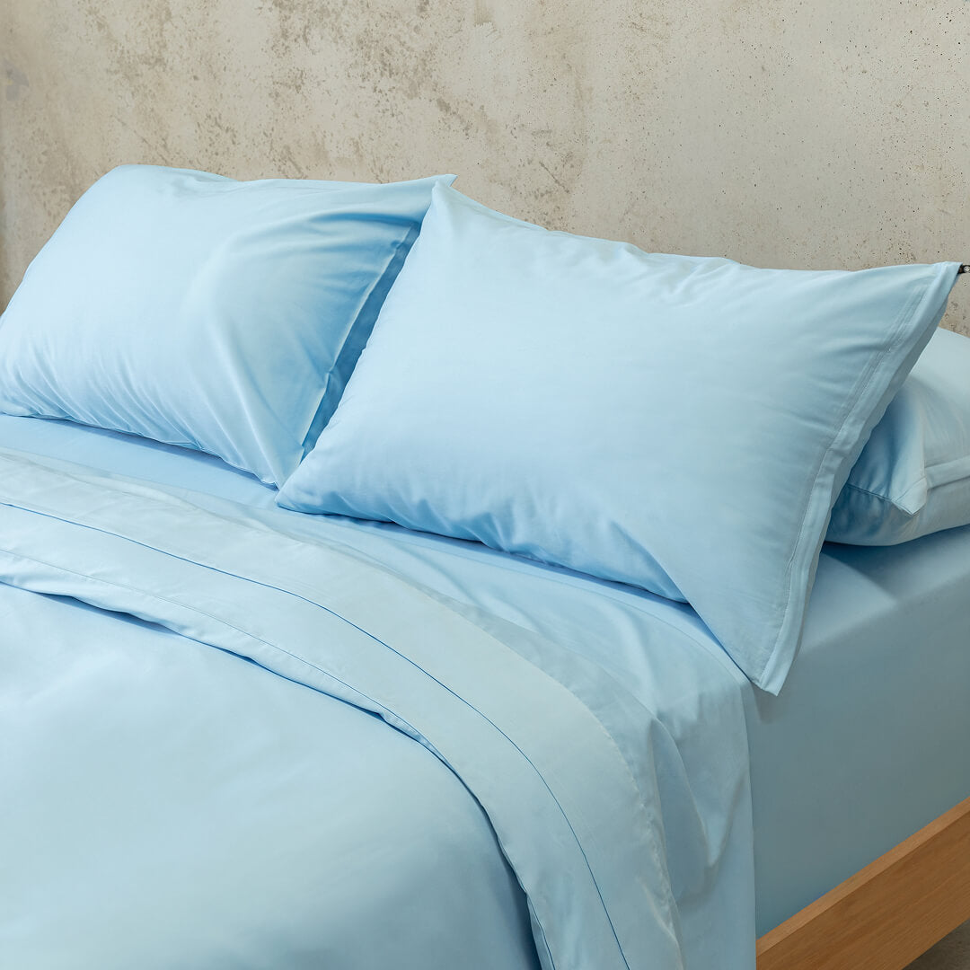 Pastel blue quilt cover set close up on a bed, with a neutral background. 