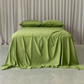 Green bedspread on a bed with matching pillows against a neutral curtain background.