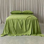 Green bedspread on a bed with matching pillows against a neutral curtain background.