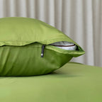 Green pillow with zipper on a bed against a neutral curtain background.