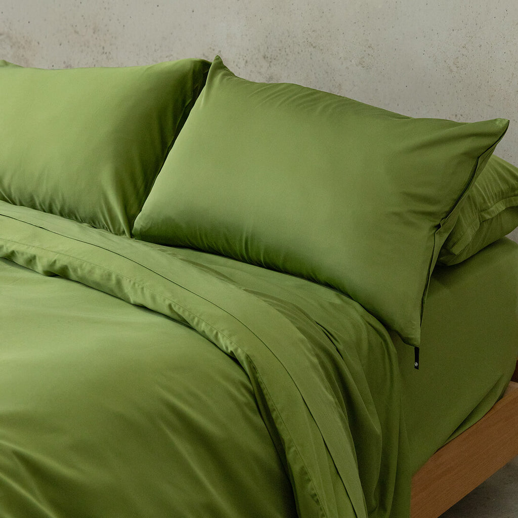 Green bedding set on a bed with a neutral background.