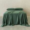 Green bedspread and pillows on a bed against a beige wall.
