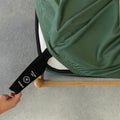 Person pulling labelled corner loop strap on green fitted sheet.