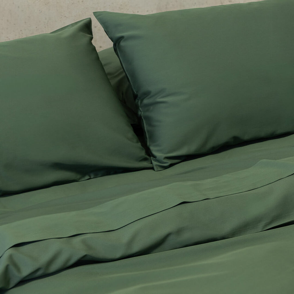 Green bed sheets and pillows on a bed with a neutral background.