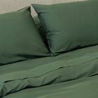 Green bed sheets and pillows on a bed with a neutral background.