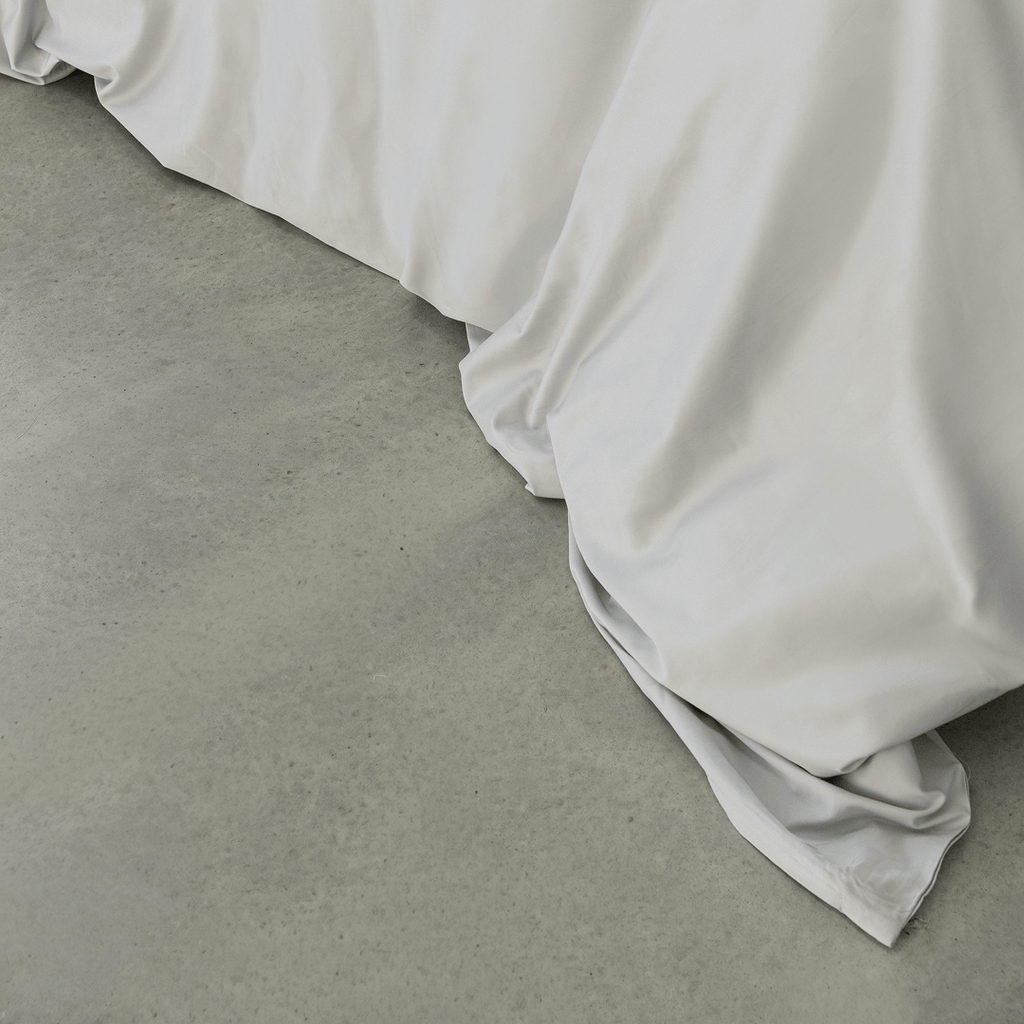 Close-up of a soft gray quilt cover draping onto a concrete floor, highlighting its smooth finish and flowing folds.