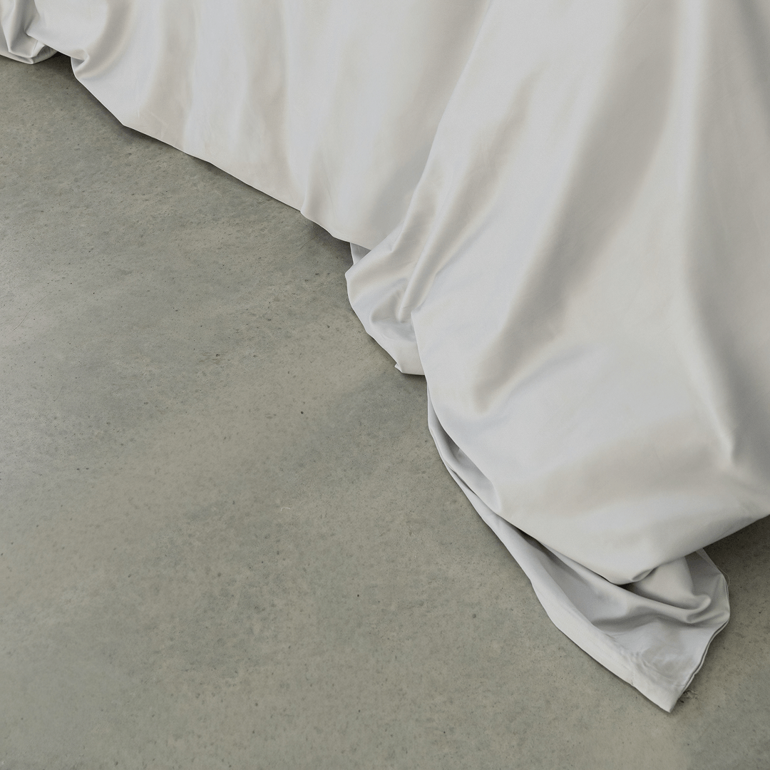 Close-up of a soft gray quilt cover draping onto a concrete floor, highlighting its smooth finish and flowing folds.