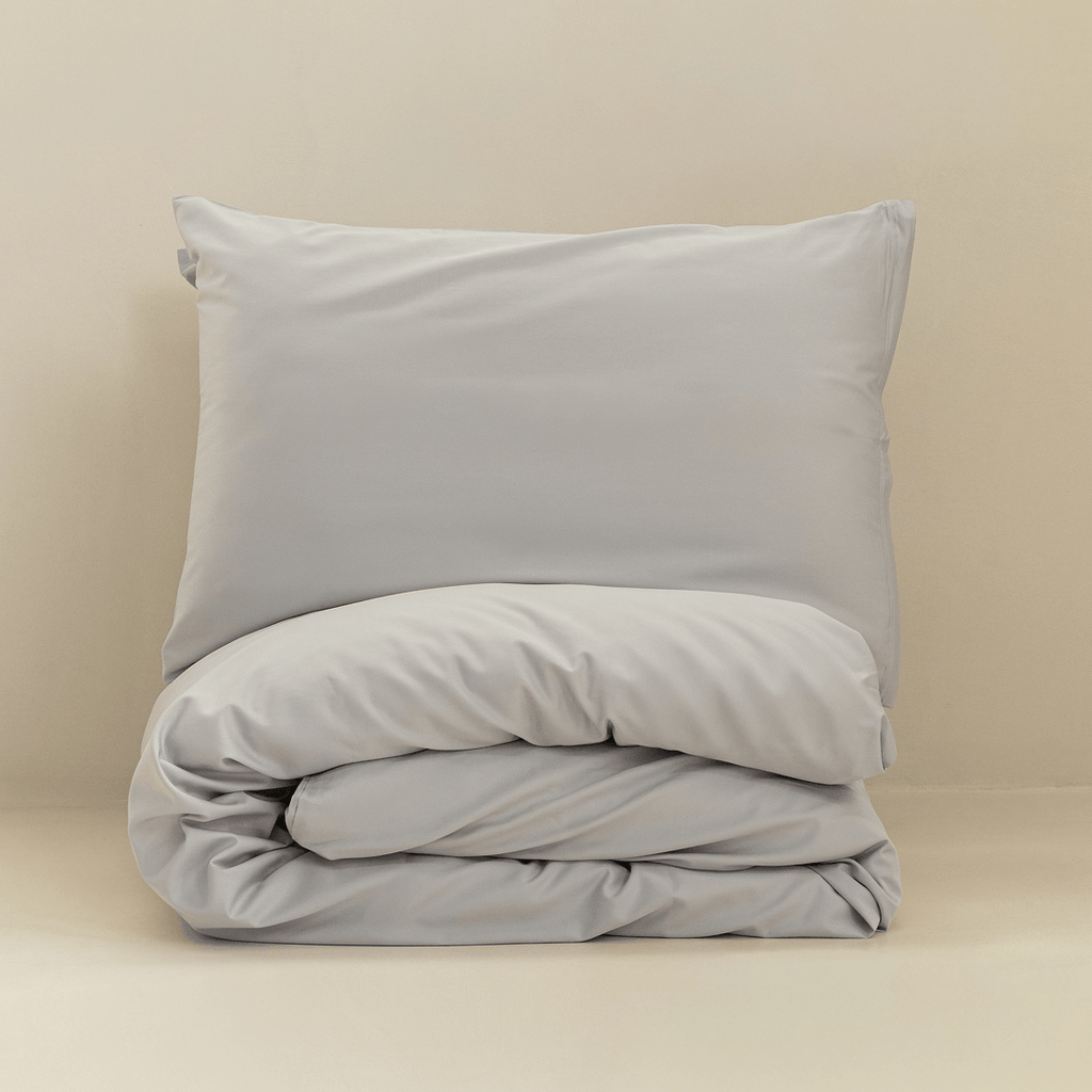 A gray pillow displayed above a neatly folded matching quilt cover against a warm neutral background.