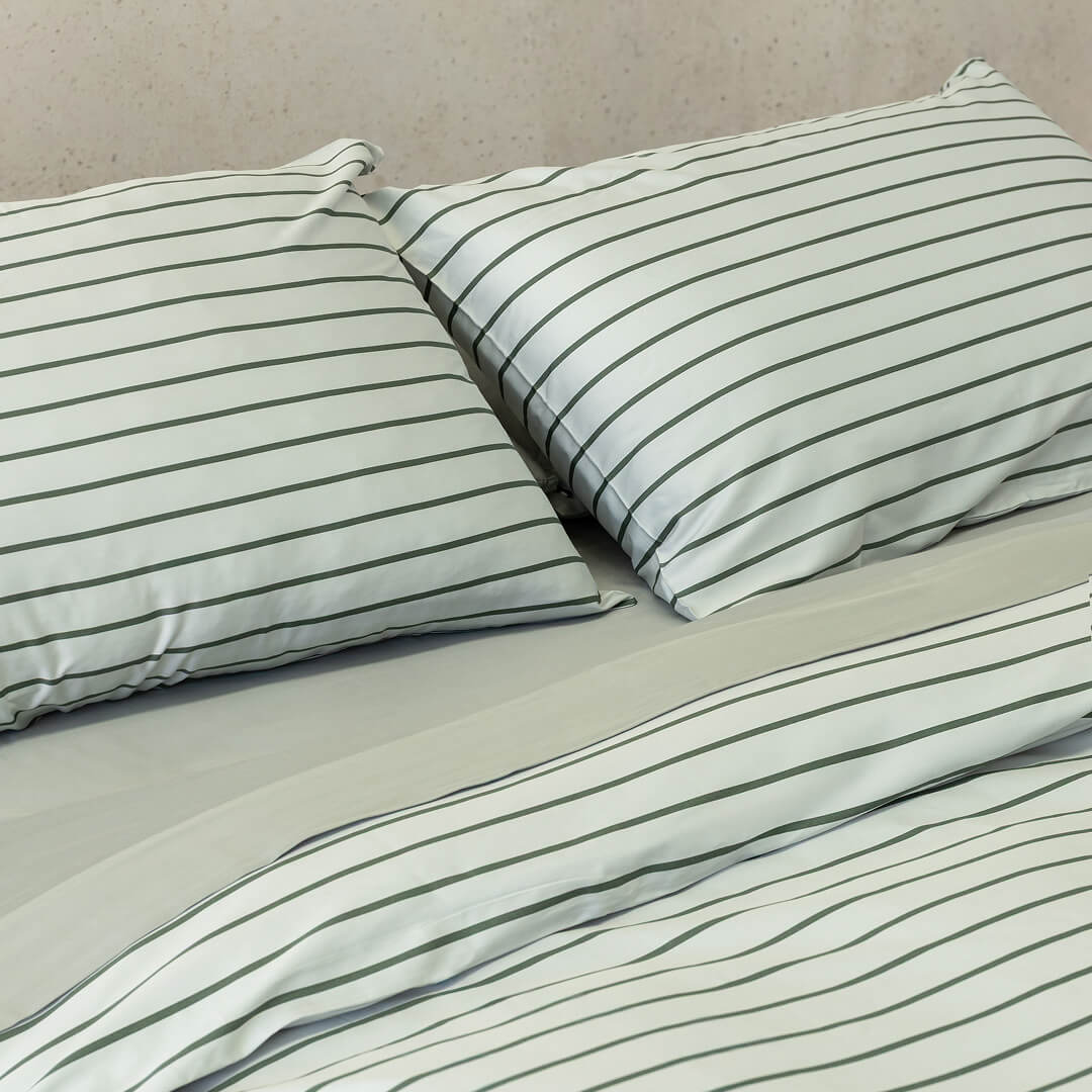 Striped pillowcases and duvet cover on a bed with beige bedding.