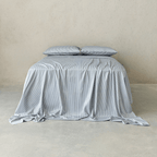 Front view of a bed dressed in gray and white pinstripe bedding with two matching pillows and a softly draped sheet against a neutral concrete wall.