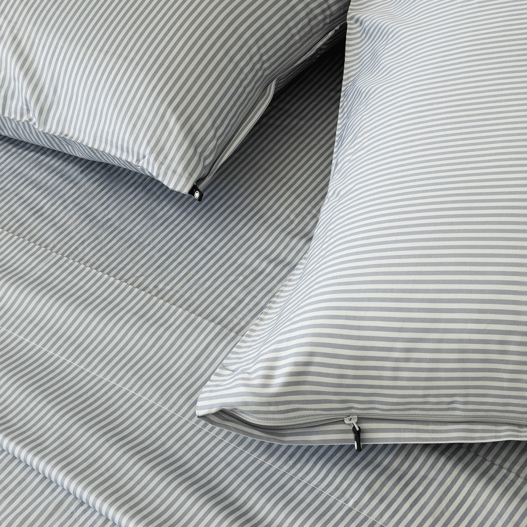 Close-up of gray and white striped pillowcases with concealed zipper closures and small black zipper pulls on matching bedding.