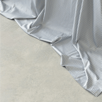 Close-up of a gray and white striped flat sheet draping softly onto a concrete floor, showing its smooth texture and flowing folds.