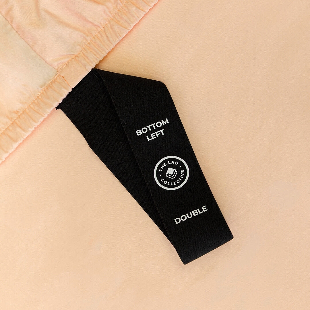 Labelled corner loop strap on peach coloured fitted sheet.