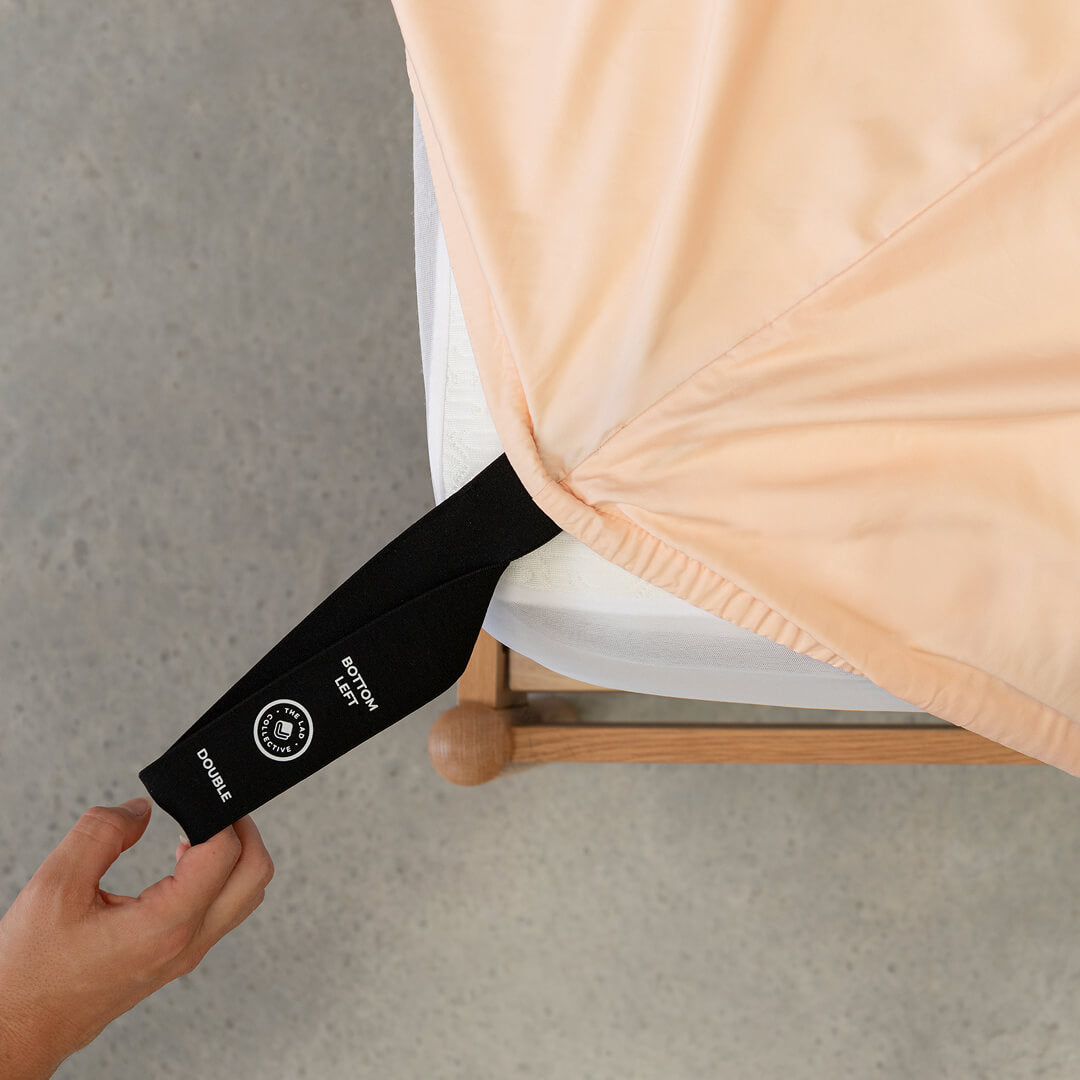 Hand pulling the fitted sheet labelled corner loop strap onto the mattress.  