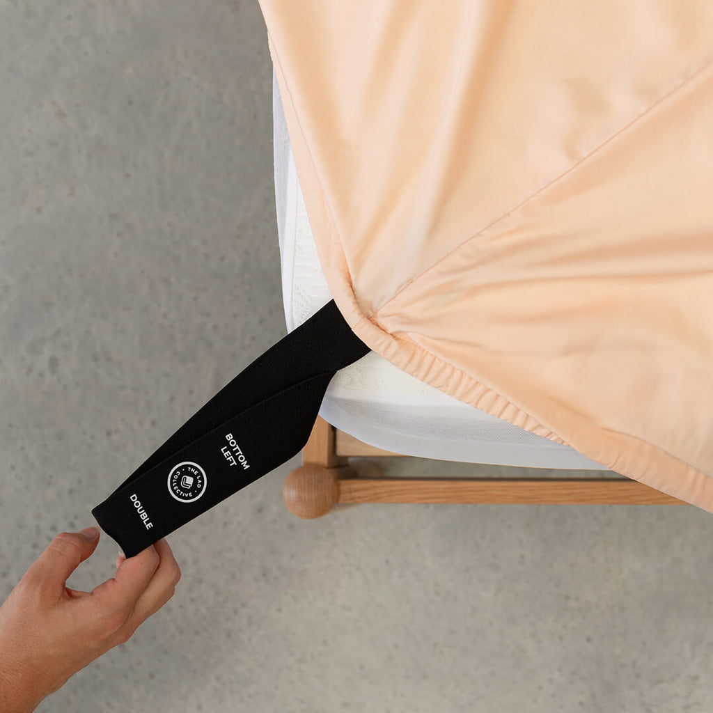 Hand pulling the fitted sheet labelled corner loop strap onto the mattress.  