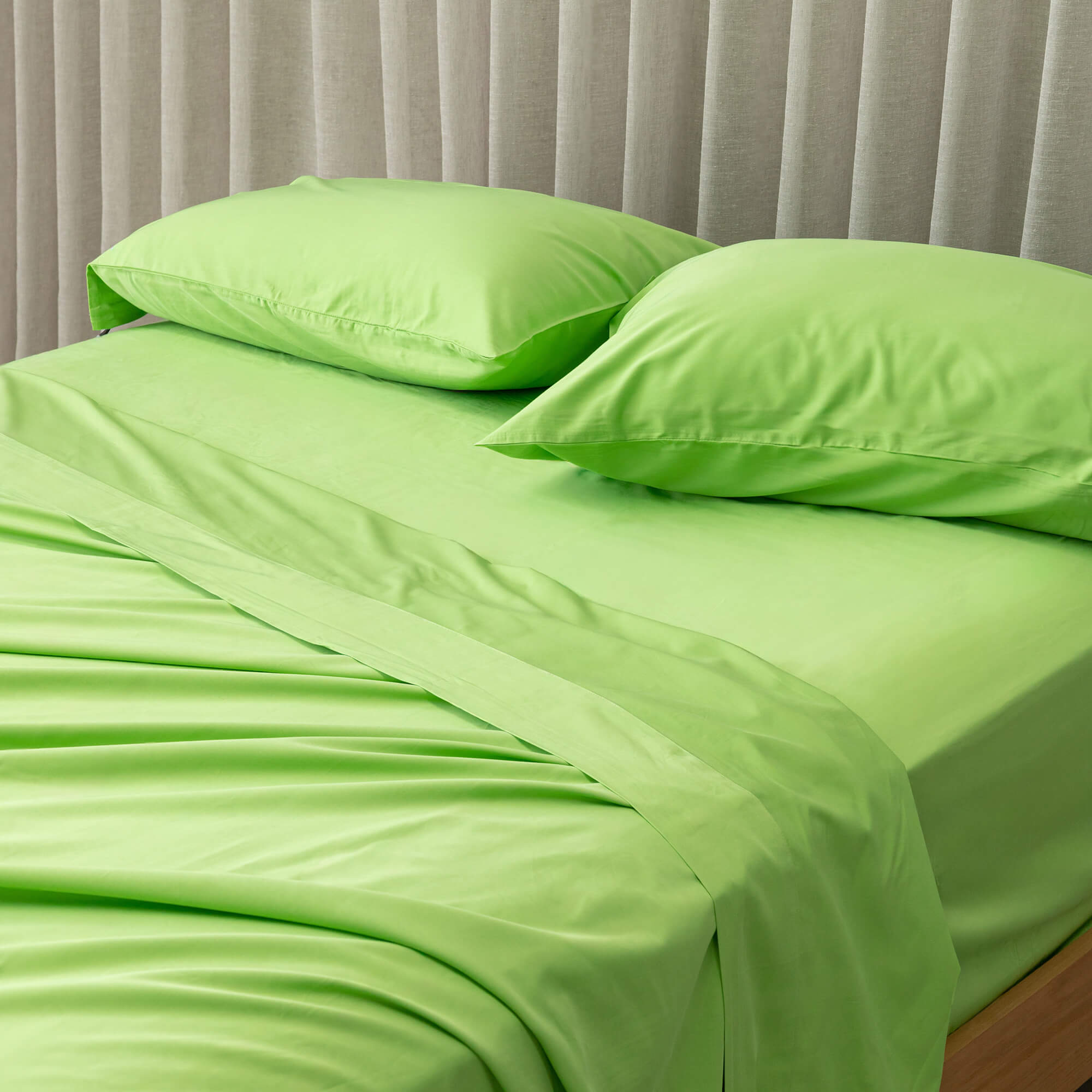 Close-up of a lime green bedding set showcased on a bed, against a neutral background and a beige curtain. 