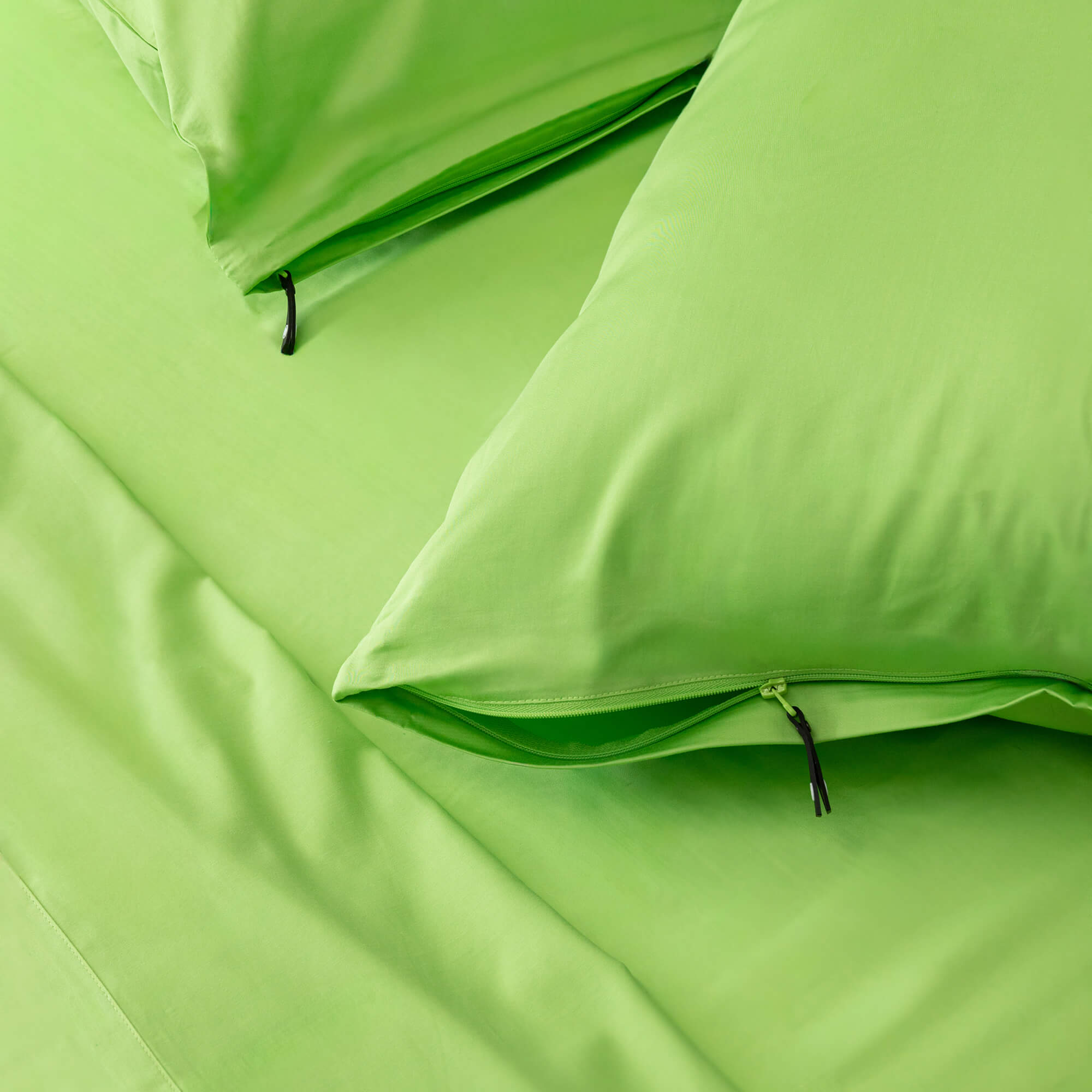 Close up of two lime-green invisible zip pillowcases on the matching bed sheets.