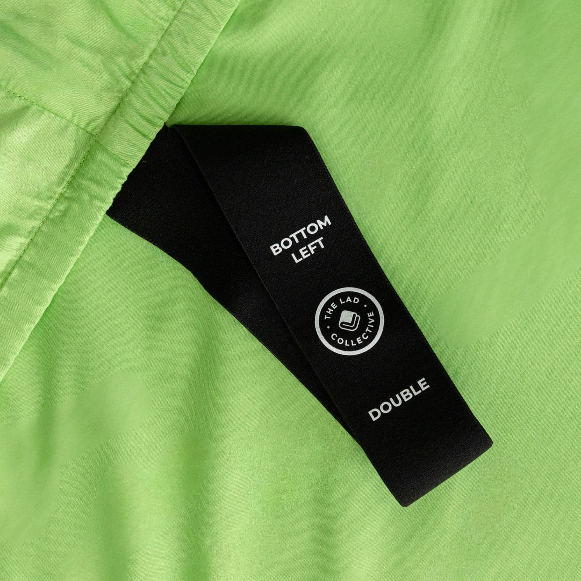Close up of our lime green fitted sheet with the labelled corner loop strap that says 'Bottom Left' and 'Double'.