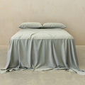 Light grey bedspread and pillows on a bed against a beige wall.