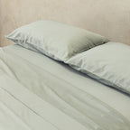 Light grey bedspread and pillows on a bed against a beige wall.