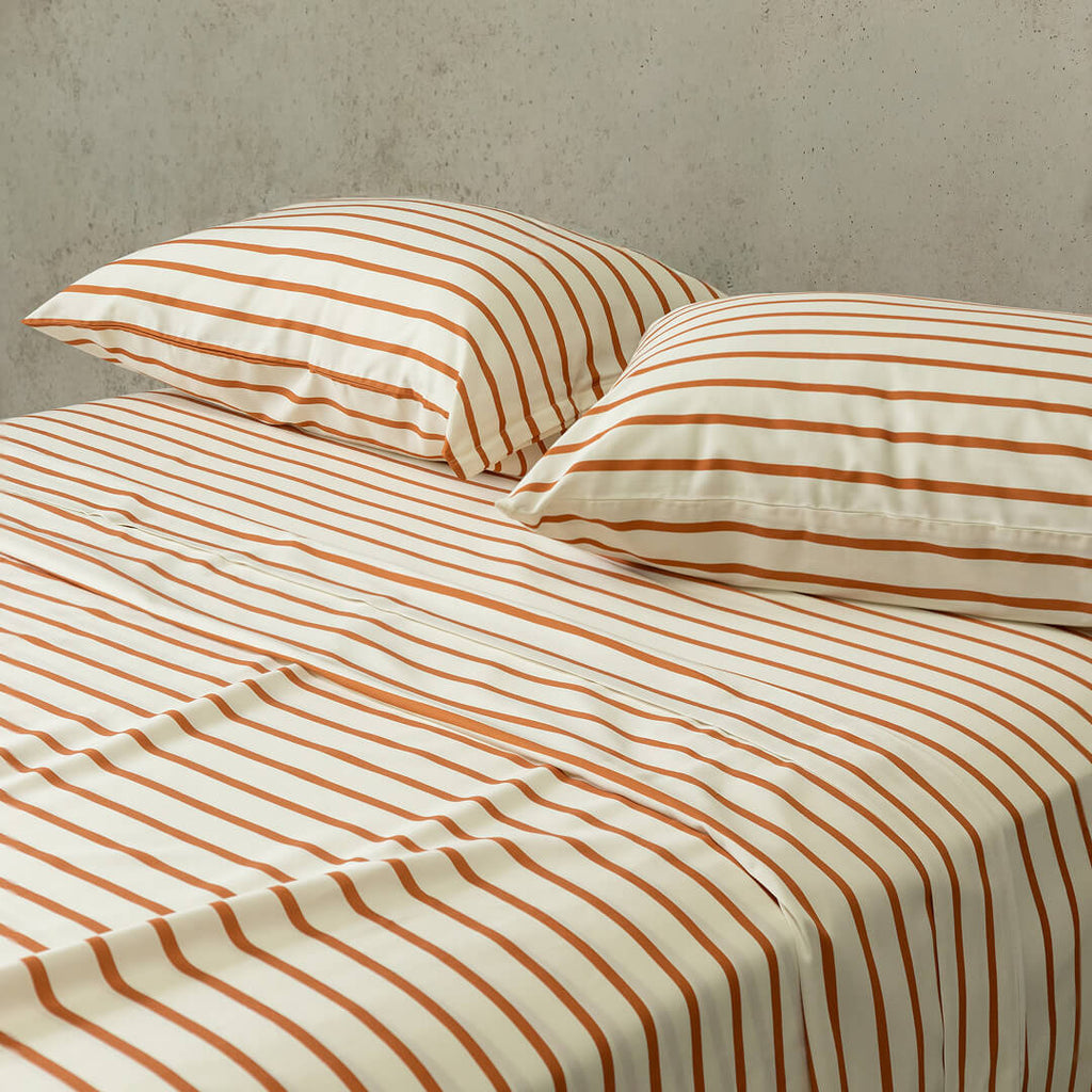 Striped bed sheets and pillows on a bed with a neutral background.