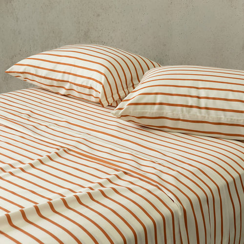 Striped bed sheets and pillows on a bed with a neutral background.