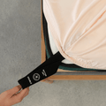 Blush pink fitted sheet with an extended orientation tag at the mattress corner, demonstrating the easy-to-locate labeling system for faster bed setup.