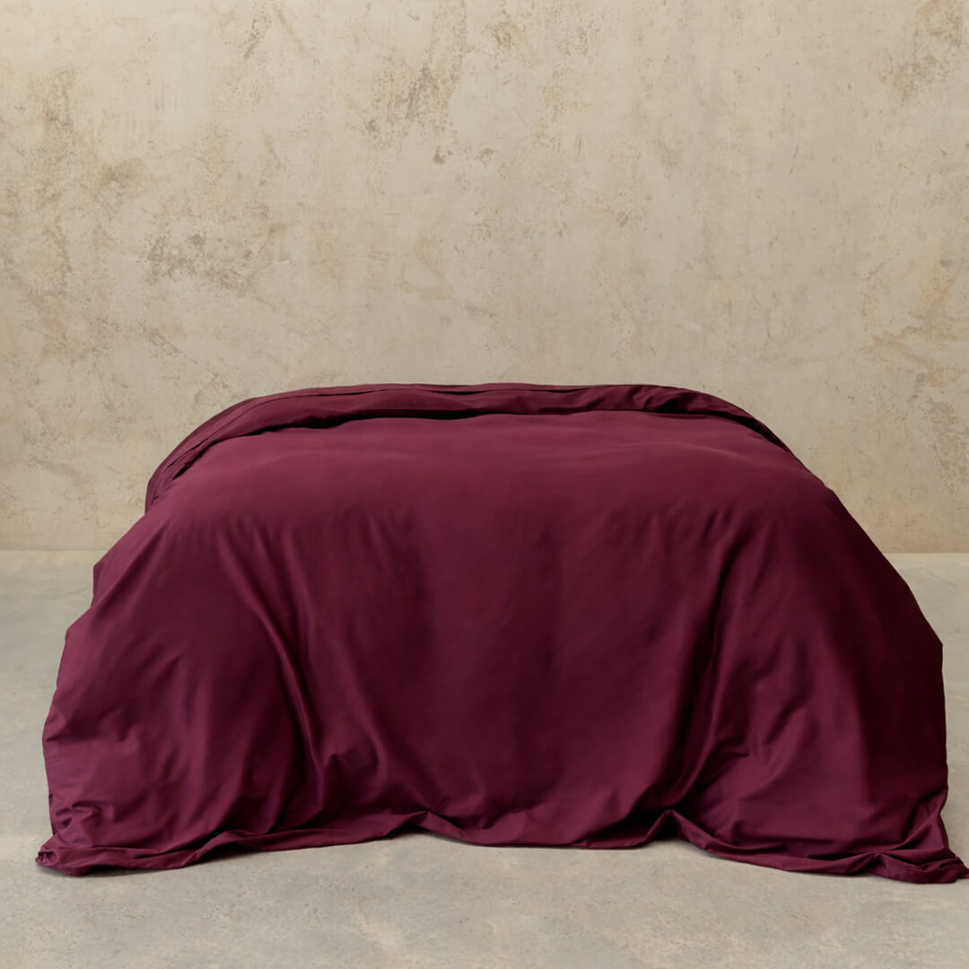 Maroon comforter on a bed against a beige wall