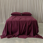 Burgundy bedspread and pillows on a bed against a beige curtain background