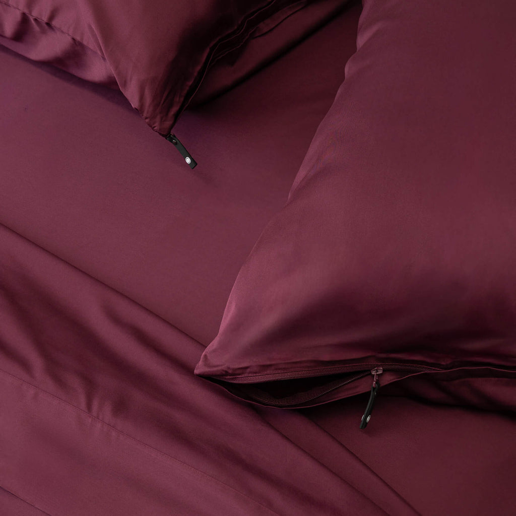 Maroon bed sheets and pillows on a bed