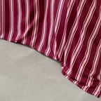 Close-up of a burgundy quilt cover with pale pink vertical stripes draping in soft folds onto a concrete floor.