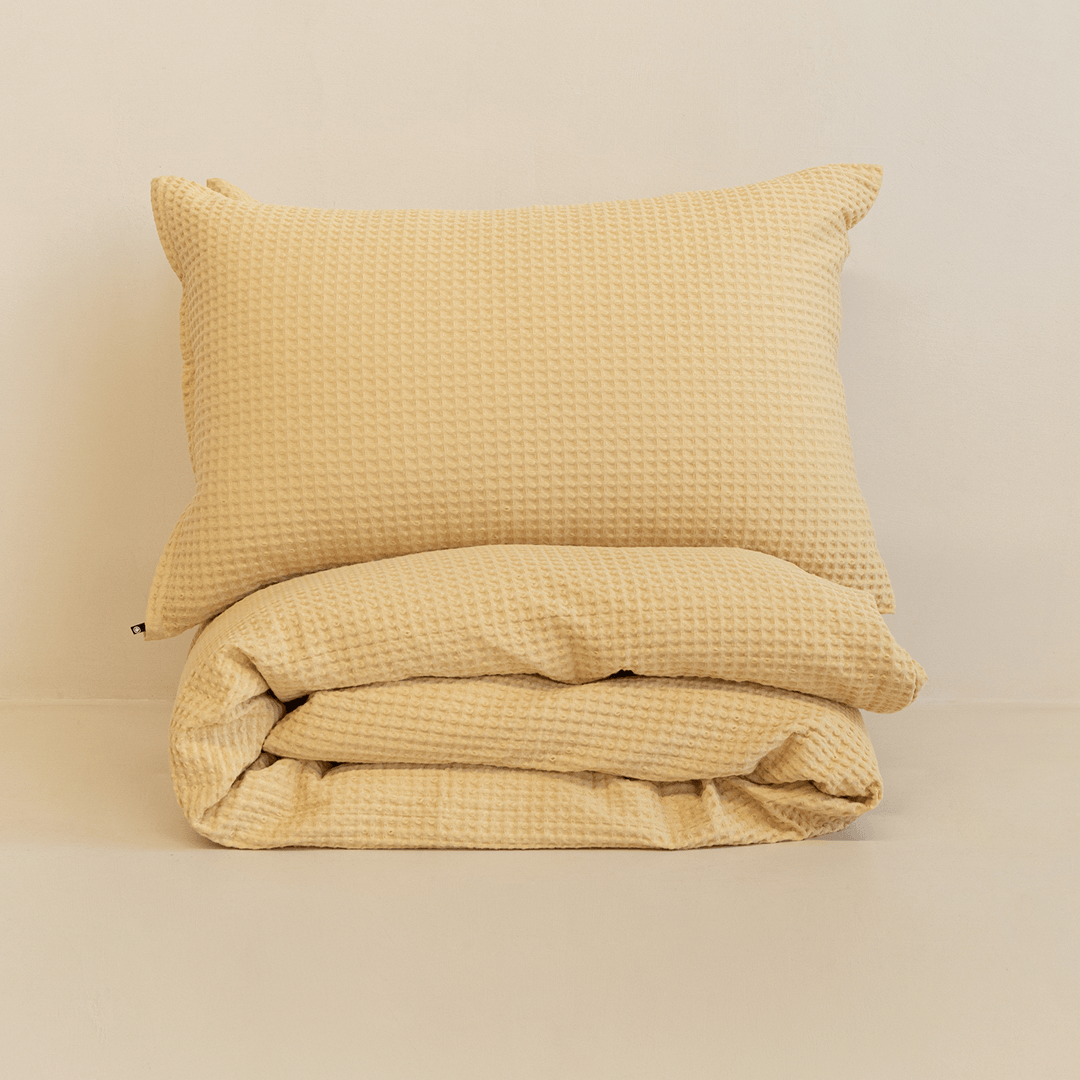 Neatly folded yellow waffle-weave quilt with one matching pillowcase placed on top against a neutral backdrop