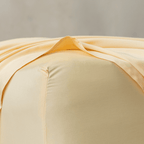 Close-up corner detail of a pale yellow fitted sheet and top flat sheet showing smooth texture and seam stitching